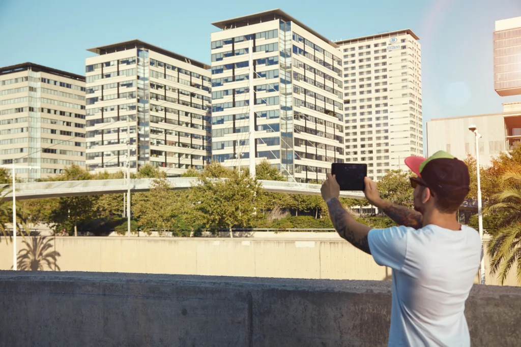 Homme prenant une photo de bâtiments modernes, représentant l'importance de l'emplacement et de la gestion des biens immobiliers